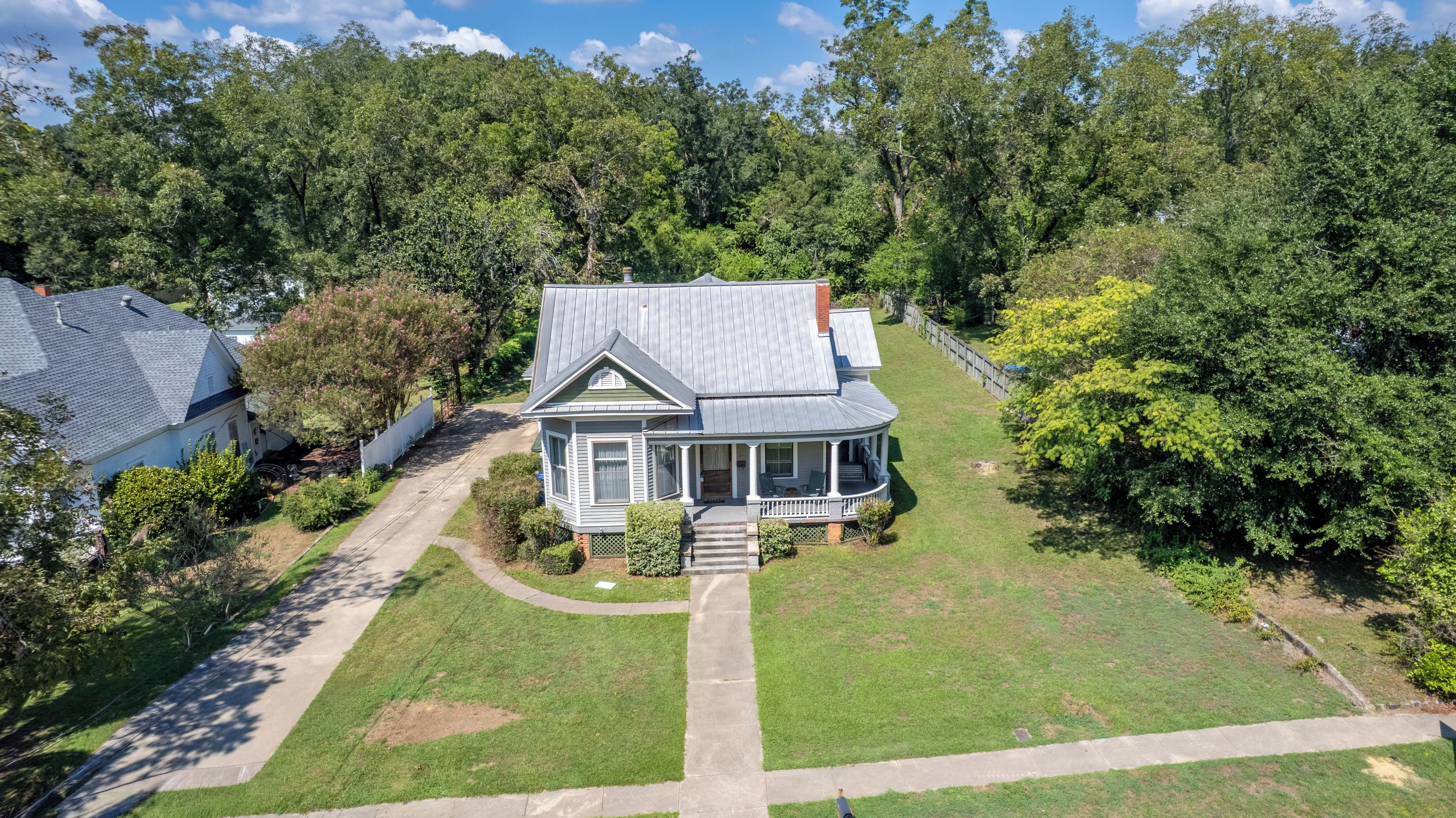 A two-story house with a porch, surrounded by a well-maintained lawn and dense trees.