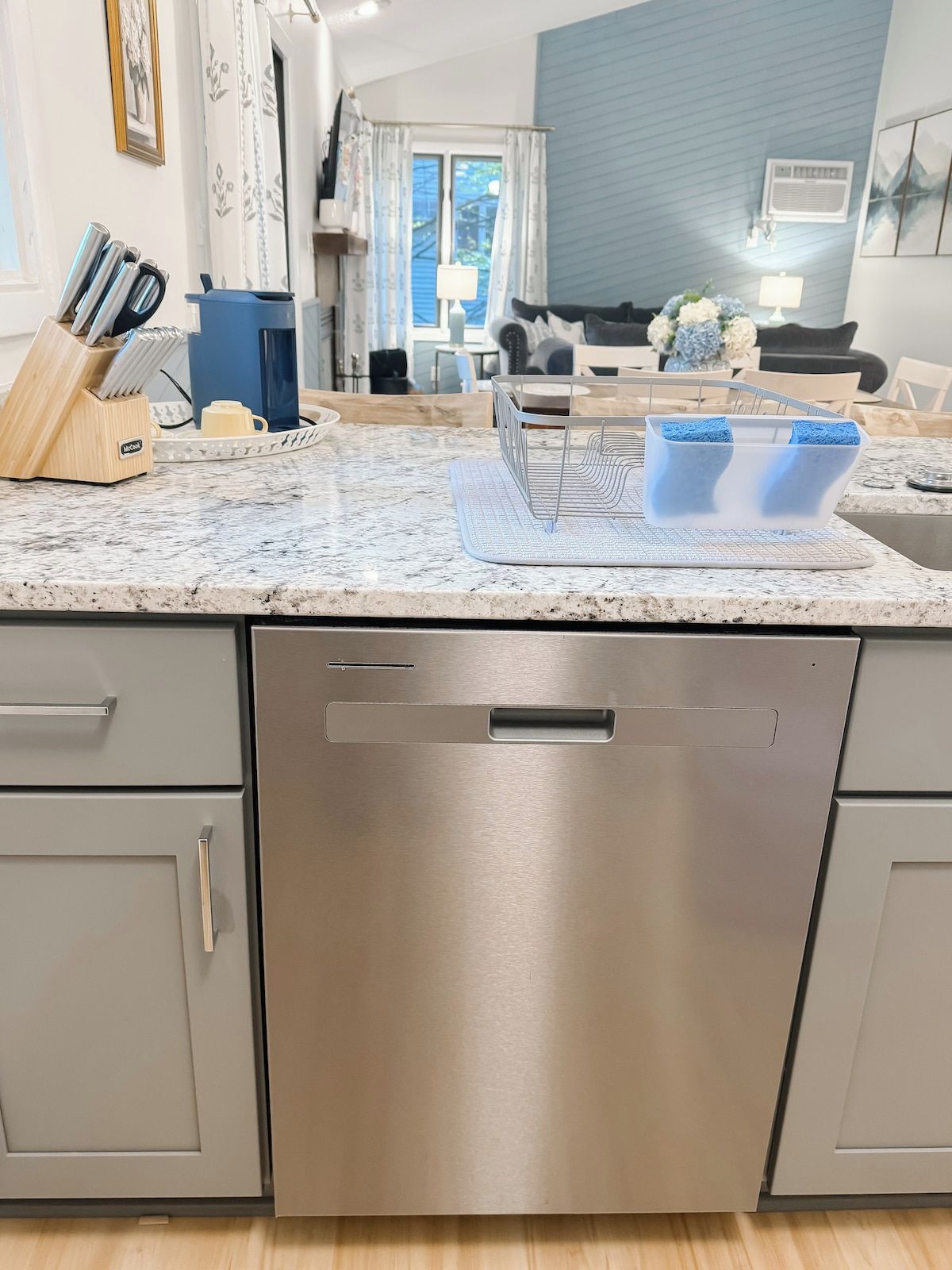 A modern kitchen with a stainless steel dishwasher, a marble countertop, and a blue kitchen mat.