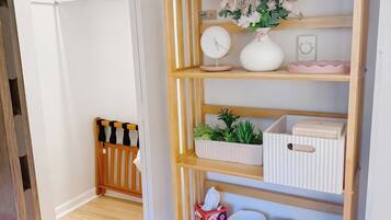A room with a wooden shelf unit containing various items, a small clock, and a vase with flowers.
