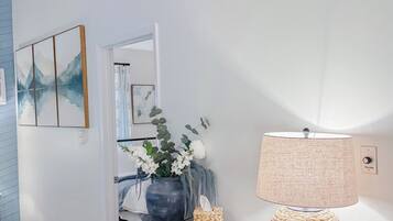 A room with a wooden console table, a lamp, a vase with flowers, and a framed picture on the wall.