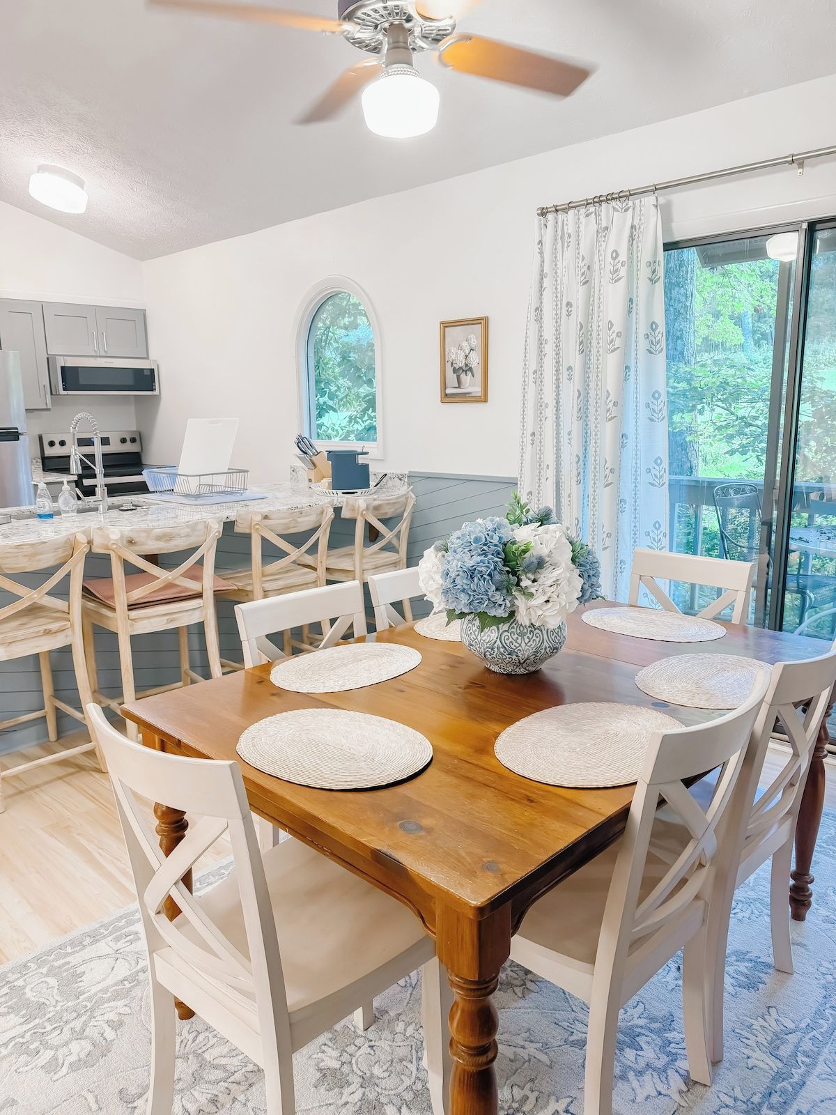 A dining area with a wooden table, white chairs, and a ceiling fan.