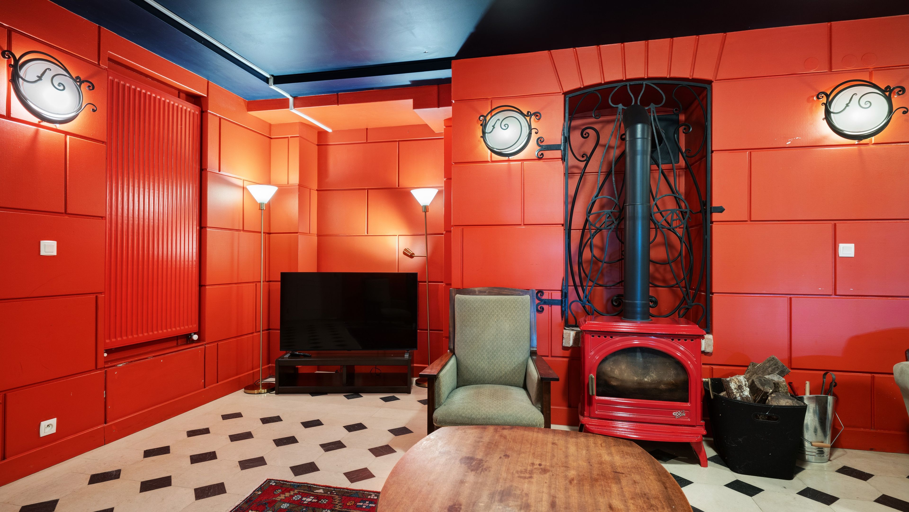 Quarto com paredes vermelhas, lareira, televisão e tapete estampado.