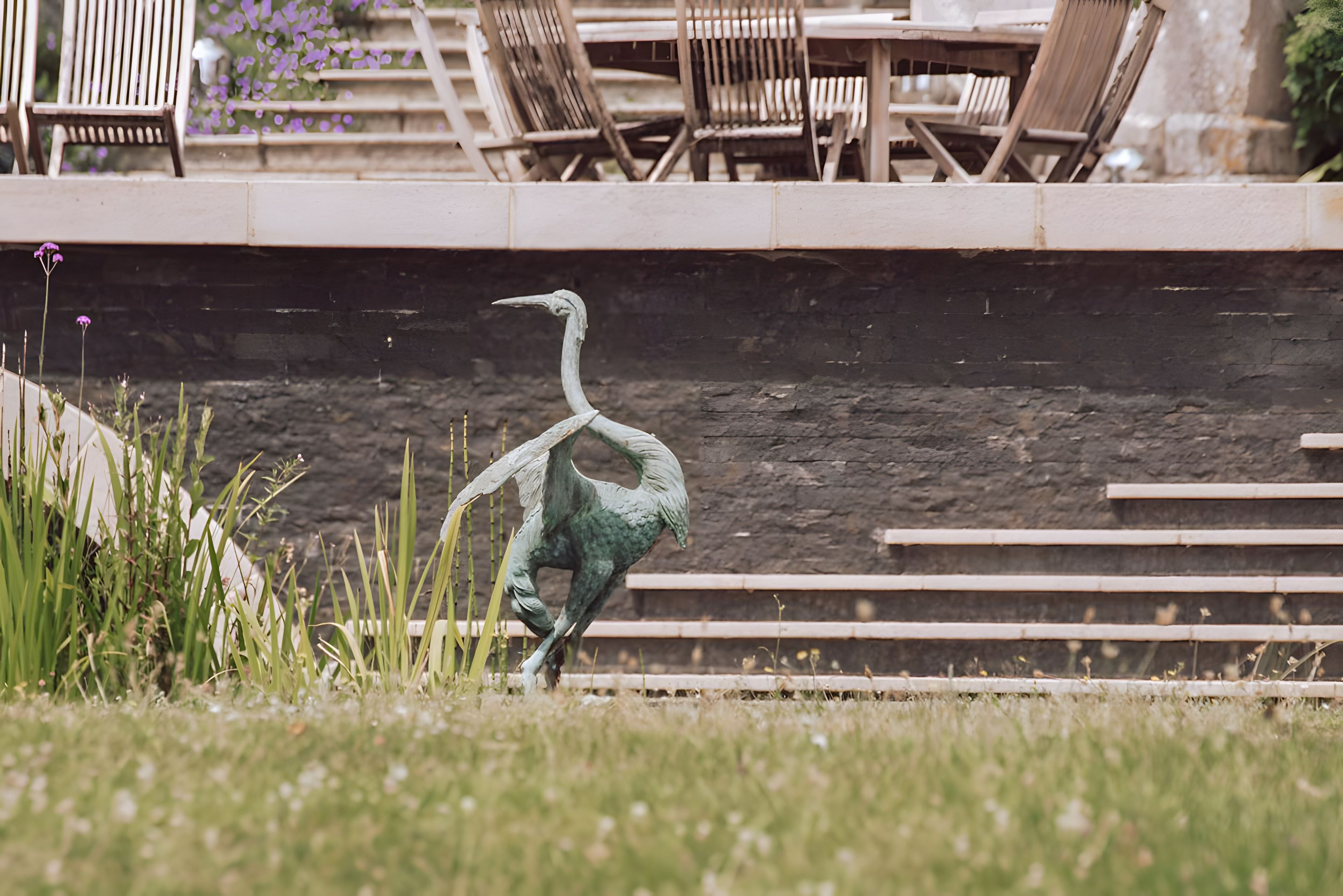 A statue of a bird in a park with steps and chairs in the background.