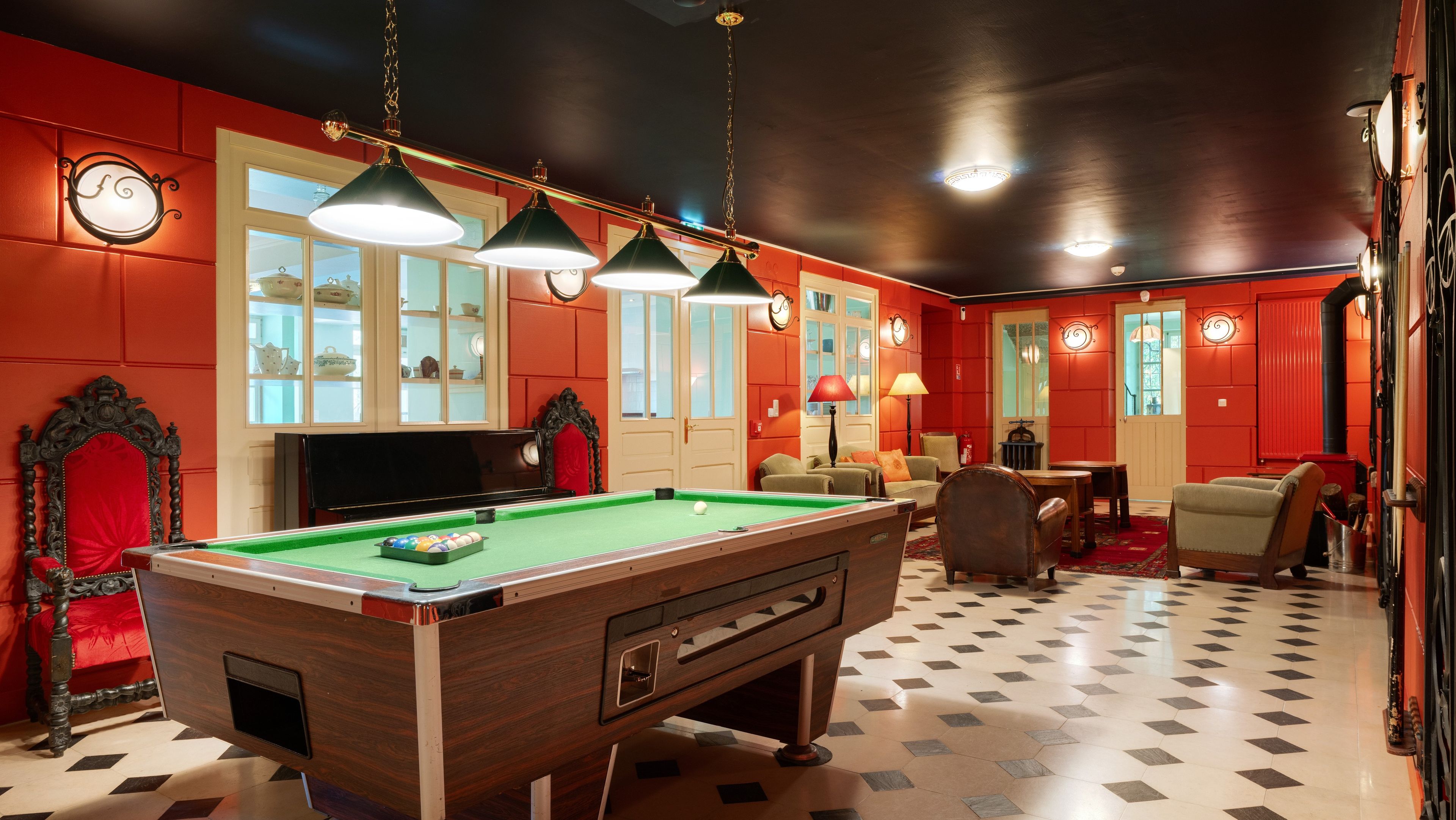 Une table de billard recouverte d’un drap vert, entourée d’une décoration rouge et noire, et un porte-queue de billard placé à côté.