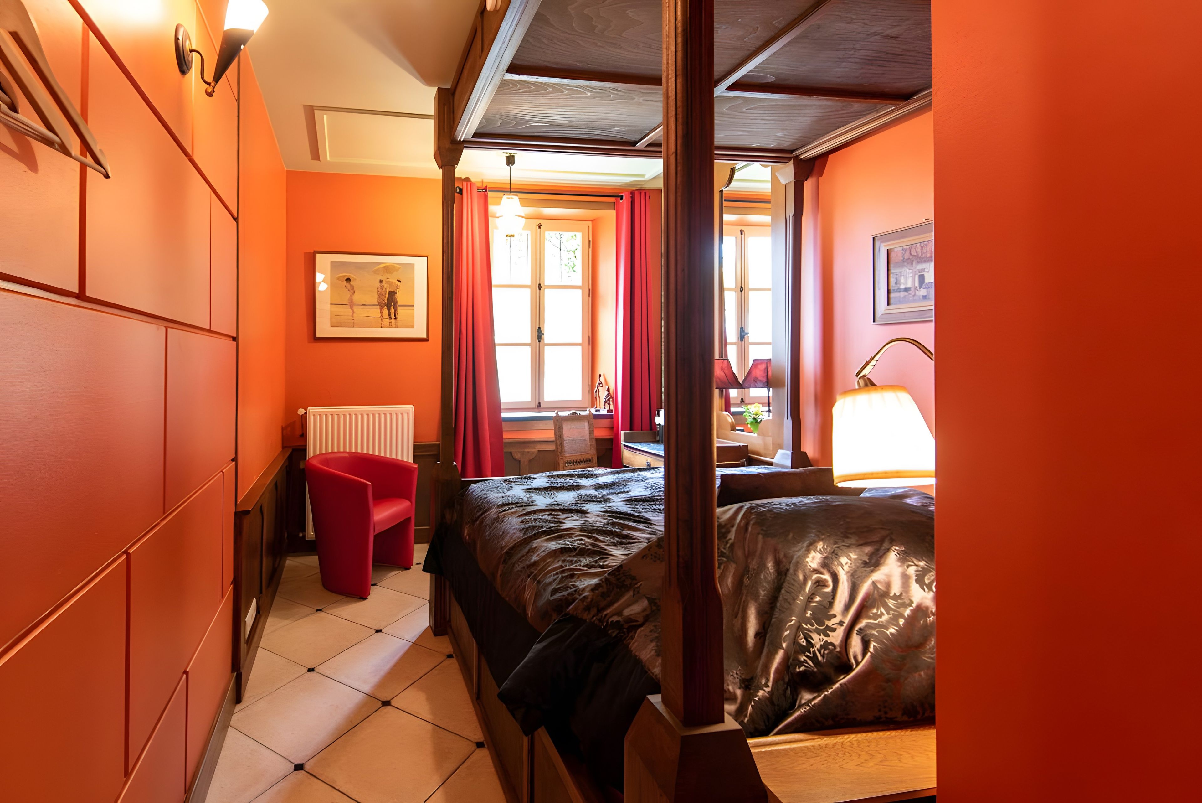 A room with a bed, a chair, a radiator, a window with curtains, and a picture on the wall.