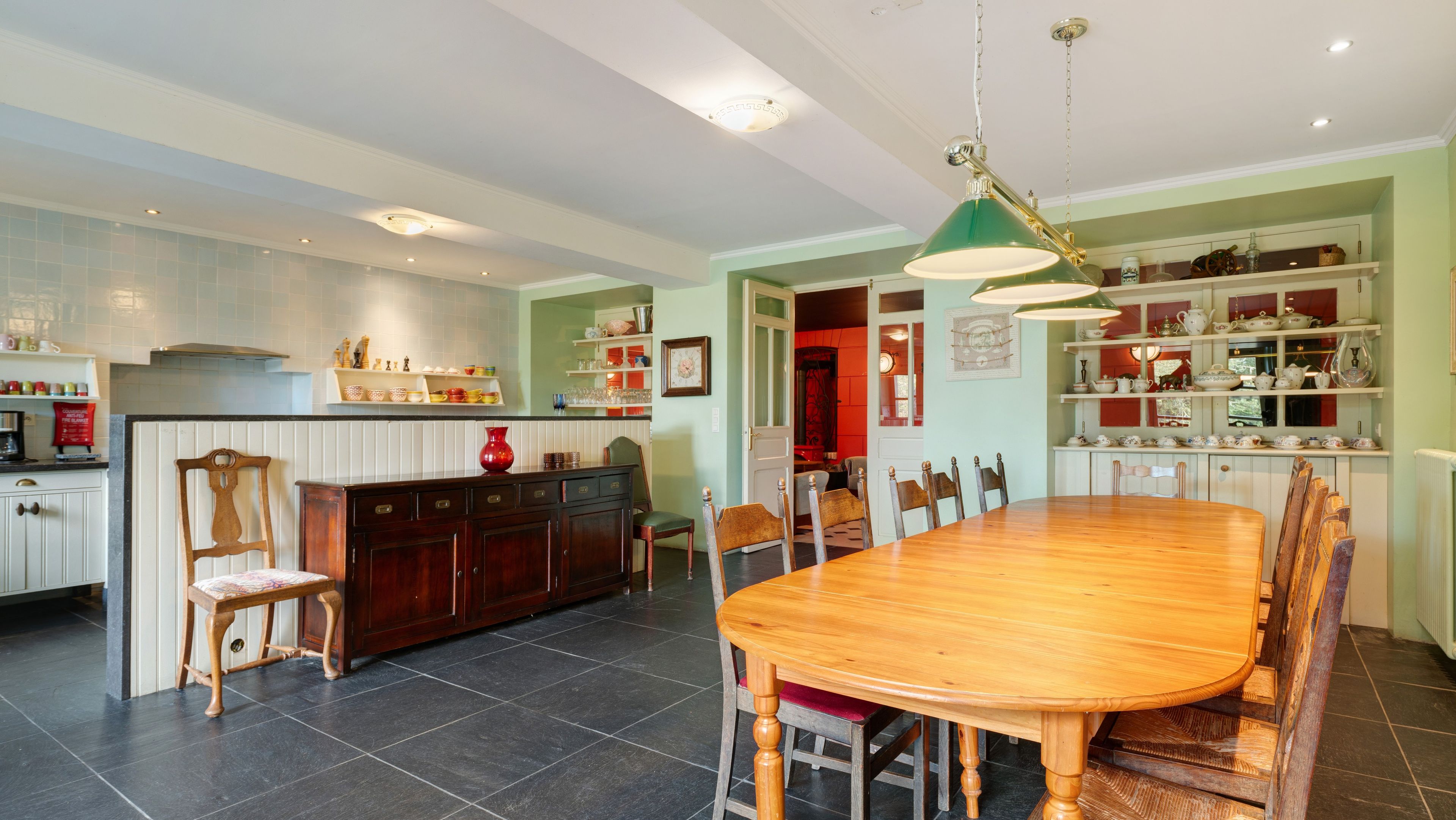 A spacious kitchen with a dining area, featuring a large wooden table and chairs, a central island with a sink, and overhead lighting.