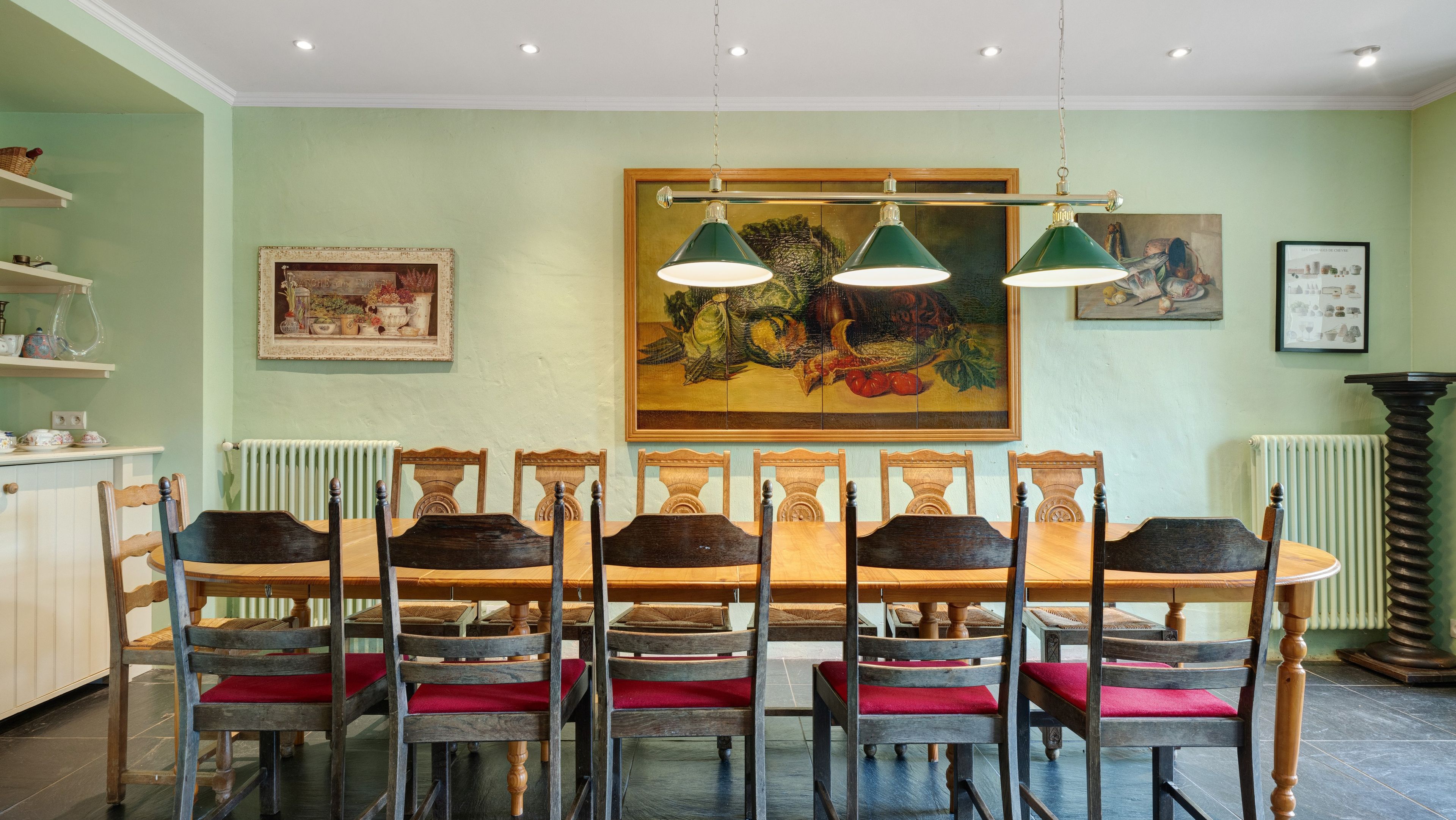 Un coin repas avec une longue table en bois et des chaises, un tableau accroché au mur et un radiateur.