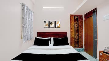 A bedroom with a bed, a wooden door, a wall-mounted light, and two framed pictures.