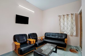 Una sala de estar con un sofá, dos sillones, una mesa de centro, un televisor de pantalla plana y una ventana con cortinas florales.