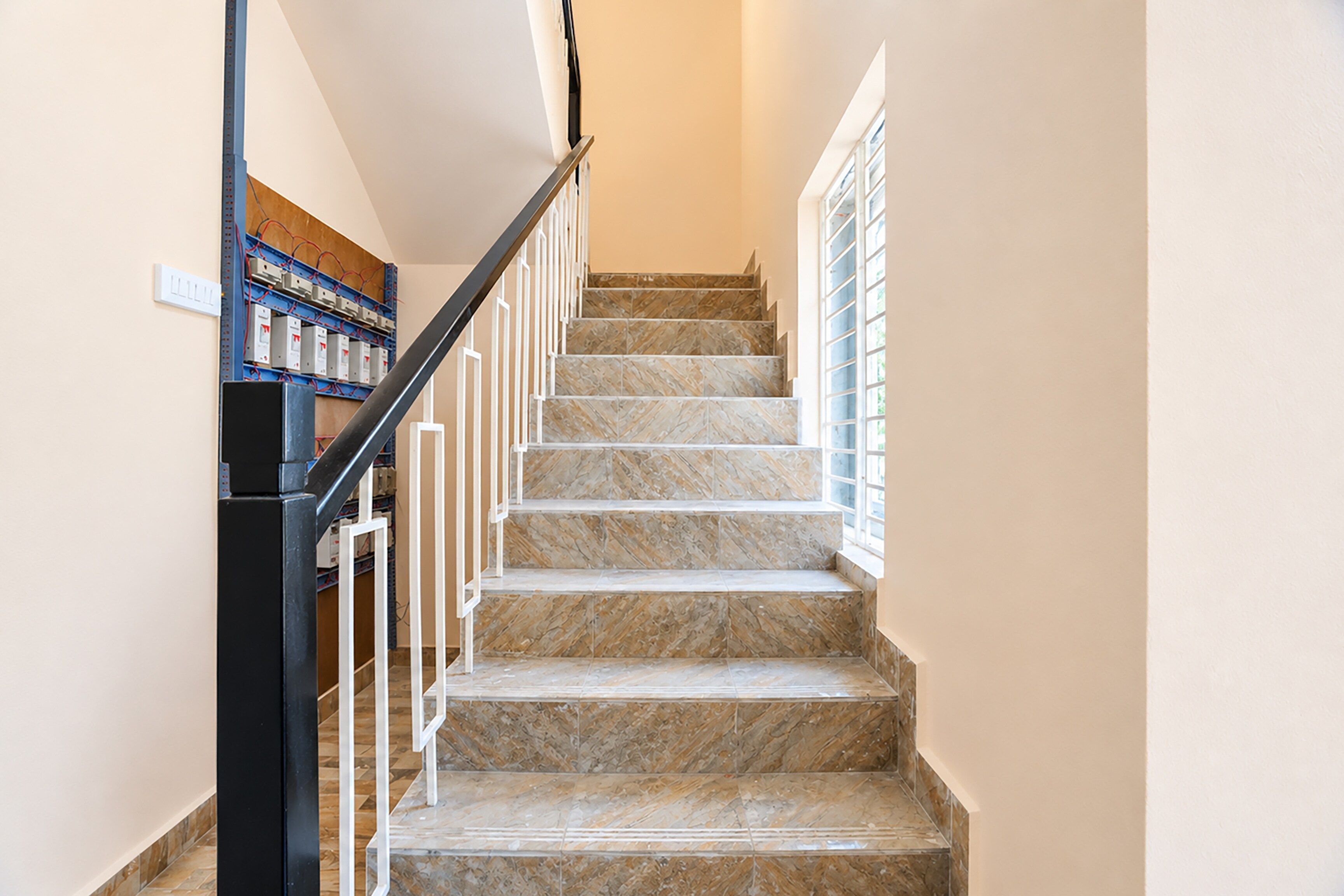 A staircase with marble steps and a metal railing, leading to a landing with a window.