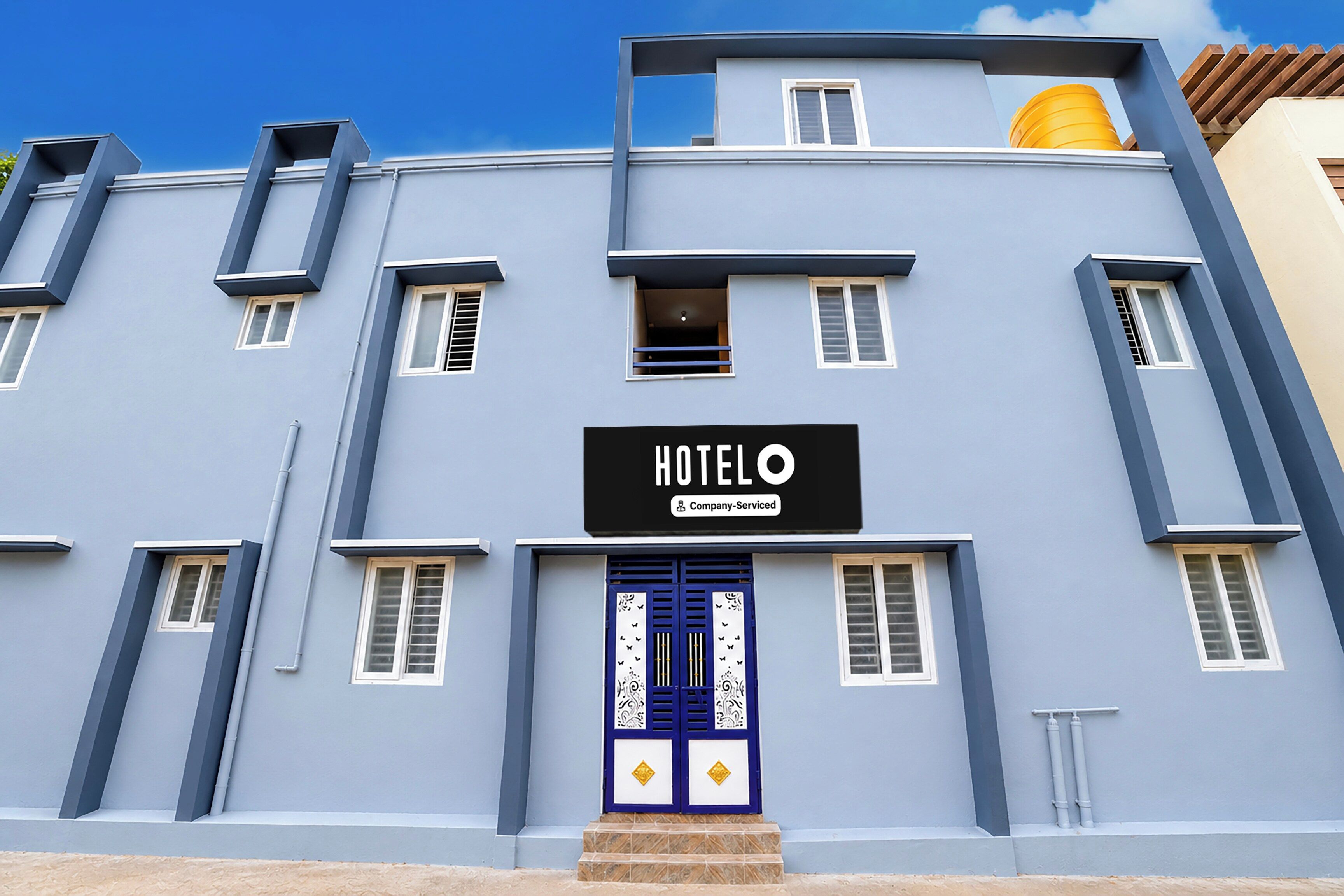 A hotel with a blue facade, a signboard with 'HOTEL' and 'Company-Serviced' text, and a blue door with decorative elements.