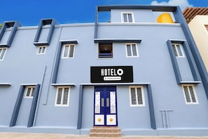 Un hotel con fachada azul, un letrero con la leyenda 'HOTEL' y 'Company-Serviced', y una puerta azul con detalles decorativos.