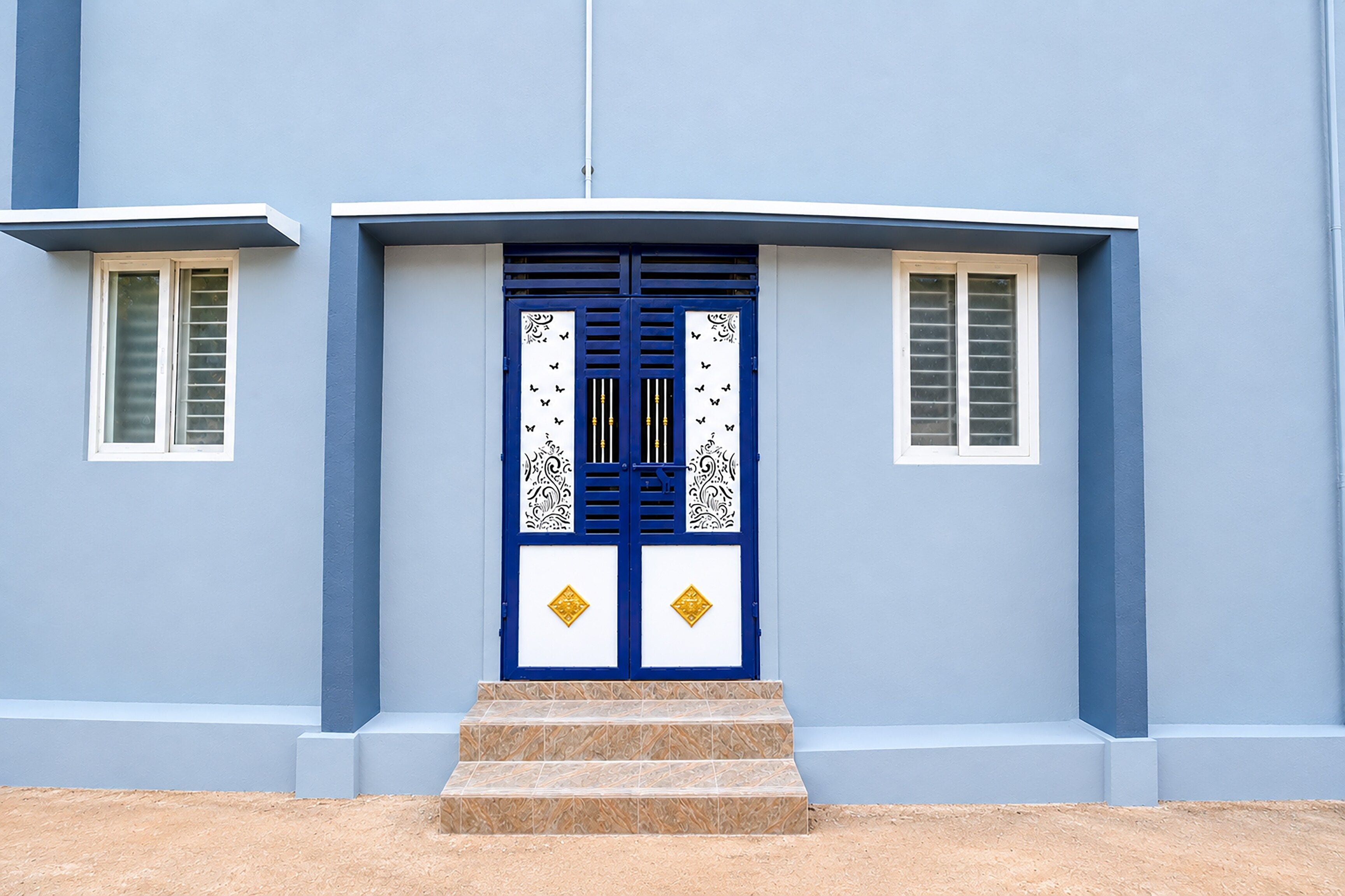 Un edificio con puerta azul, marcos de ventana blancos y una escalera que lleva a la entrada.