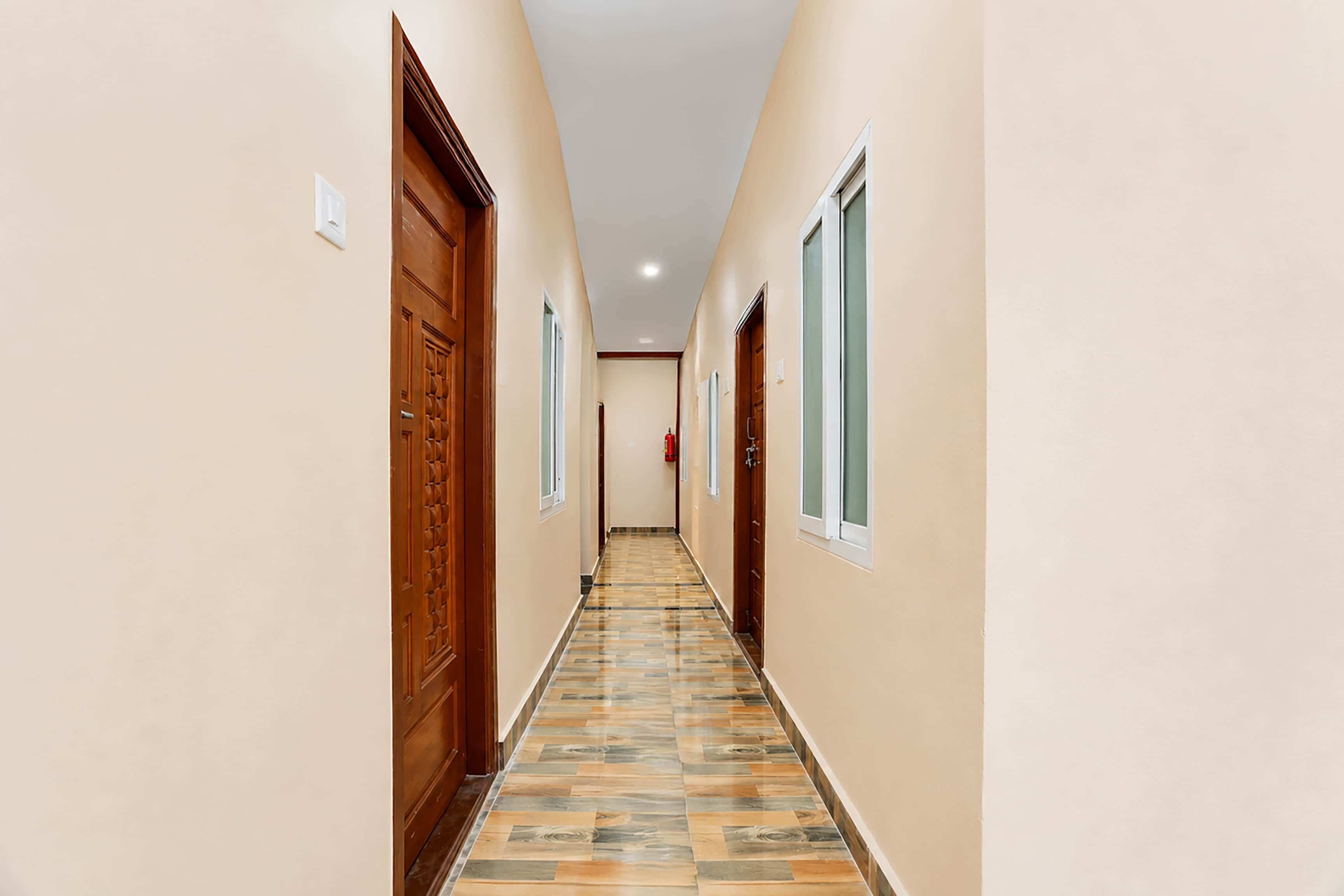 Un couloir avec des portes et des fenêtres en bois, un sol carrelé et un extincteur fixé au mur.