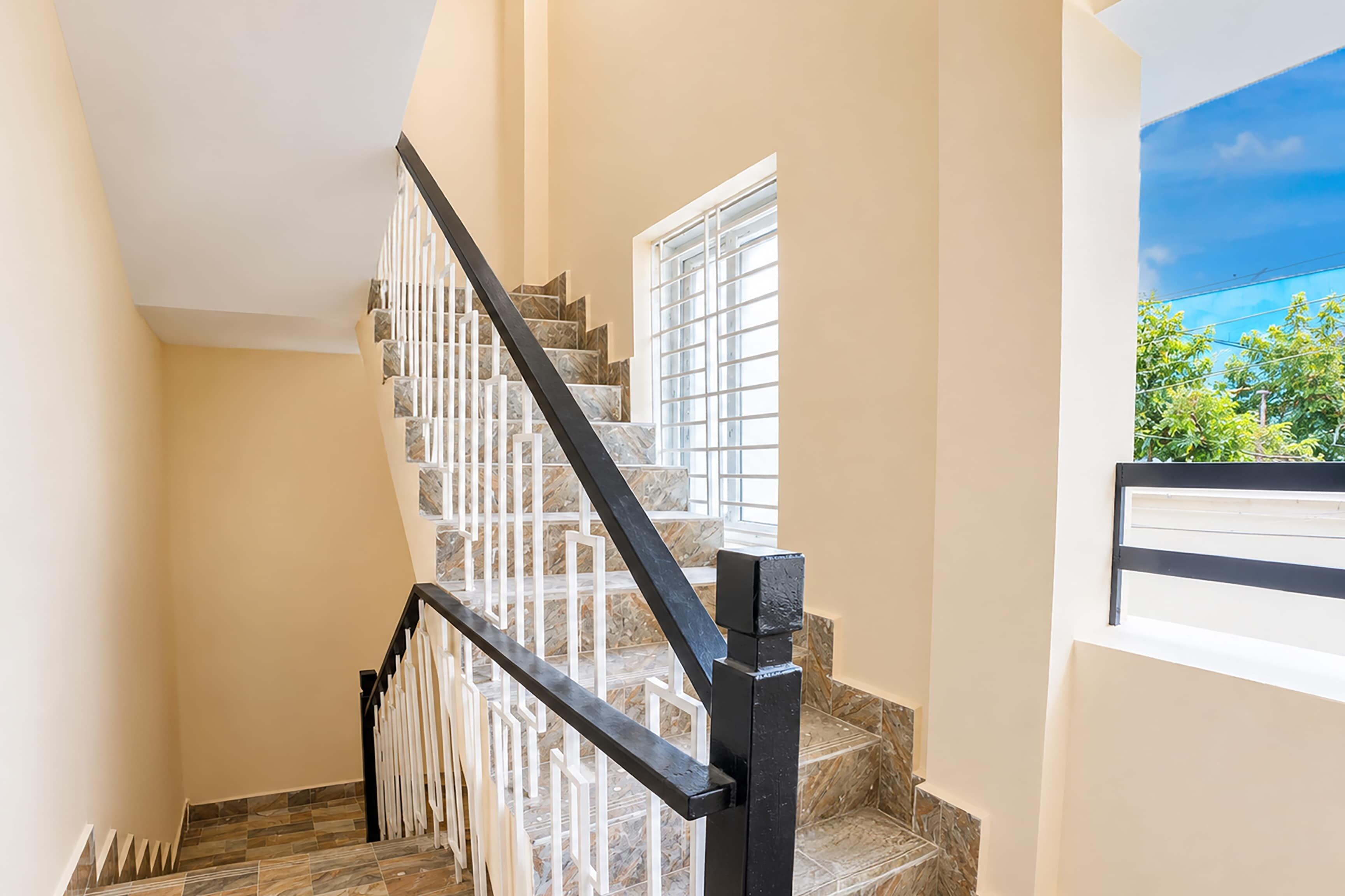 Un escalier avec une main courante noire et des balustrades blanches, menant à un palier doté d’une fenêtre.