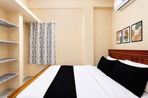 A hotel room with a bed, a wooden headboard, a window with a curtain, and a wall-mounted air conditioner.