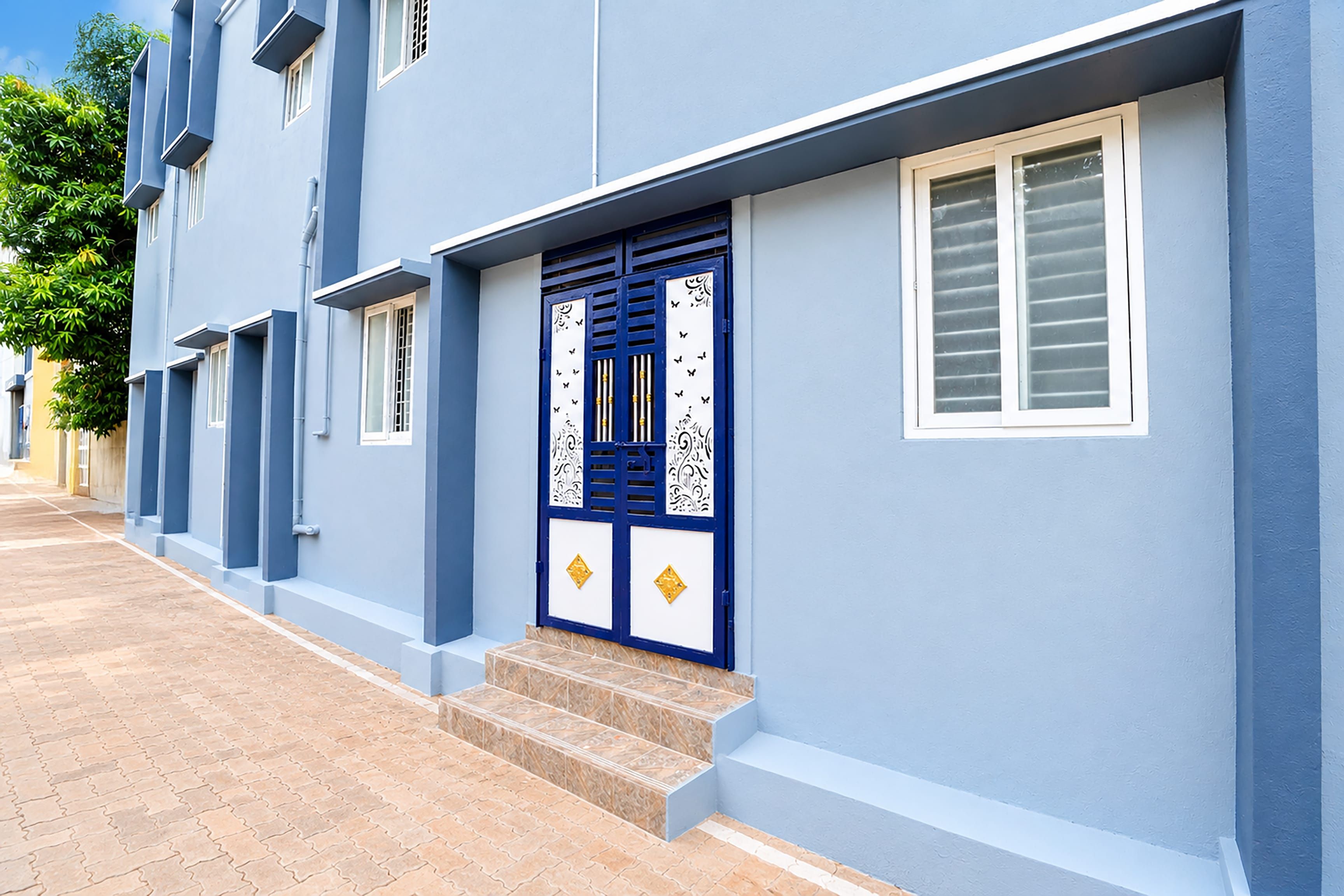 Une rangée de bâtiments modernes aux façades bleues, une porte centrale agrémentée d’éléments décoratifs et un ciel dégagé.