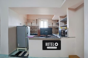 A compact kitchenette with a refrigerator, a microwave, and a small sink. There is a window providing natural light, and a sign indicating the property is serviced by a company.