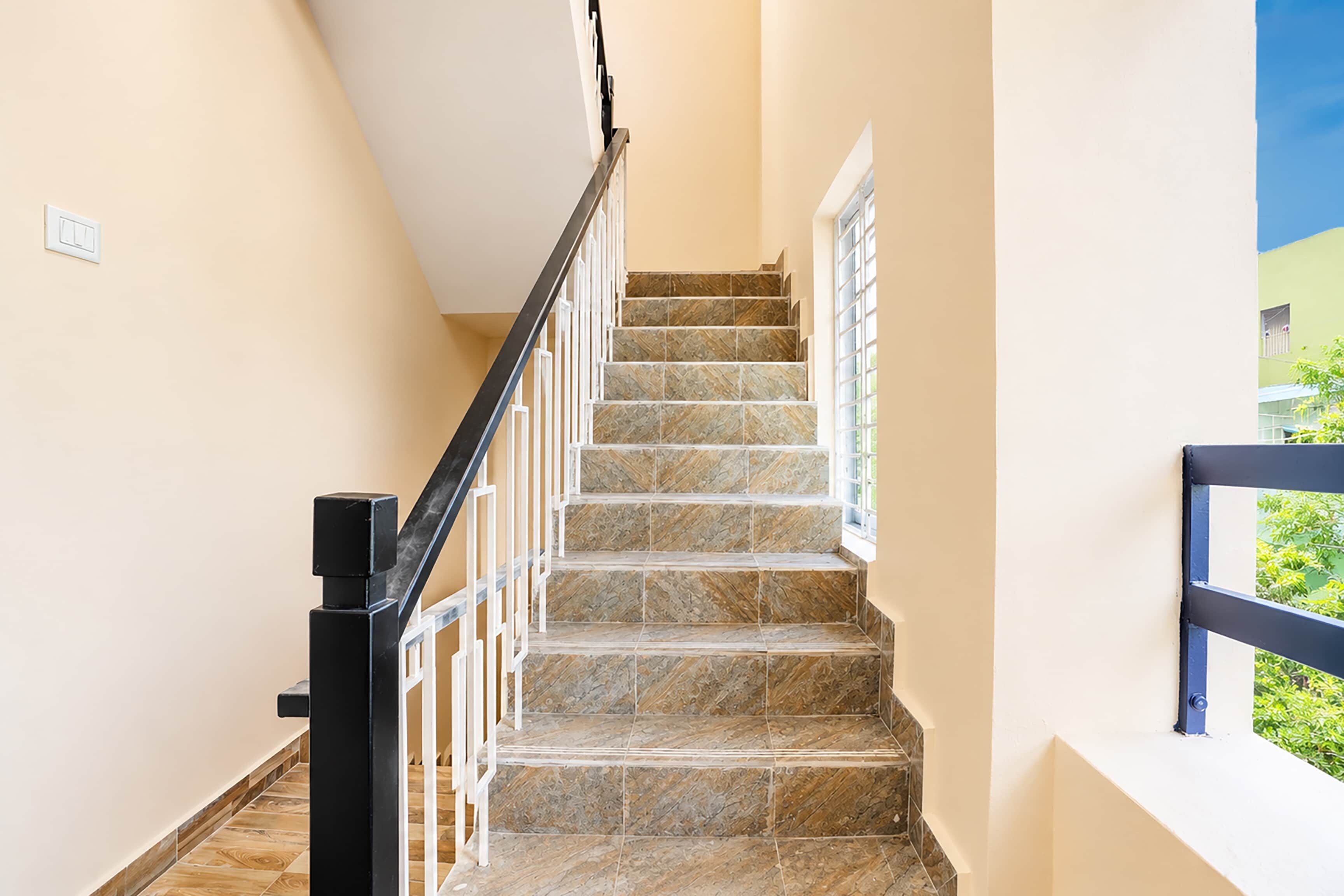 Un escalier avec des marches en pierre et une rampe noire, menant à un palier doté d’une fenêtre.