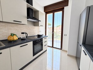 A modern kitchen with a black countertop, a stove, and a large window with a view of the outside. - De Vivo Realty - Auralis Home (Massa Lubrense)