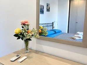 A hotel room with a bed, a bedside table with a remote control and a vase of flowers. - De Vivo Realty - Auralis Home (Massa Lubrense)
