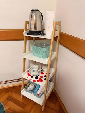 A corner shelf unit with a kettle, a basket, and a tray with cups and saucers.