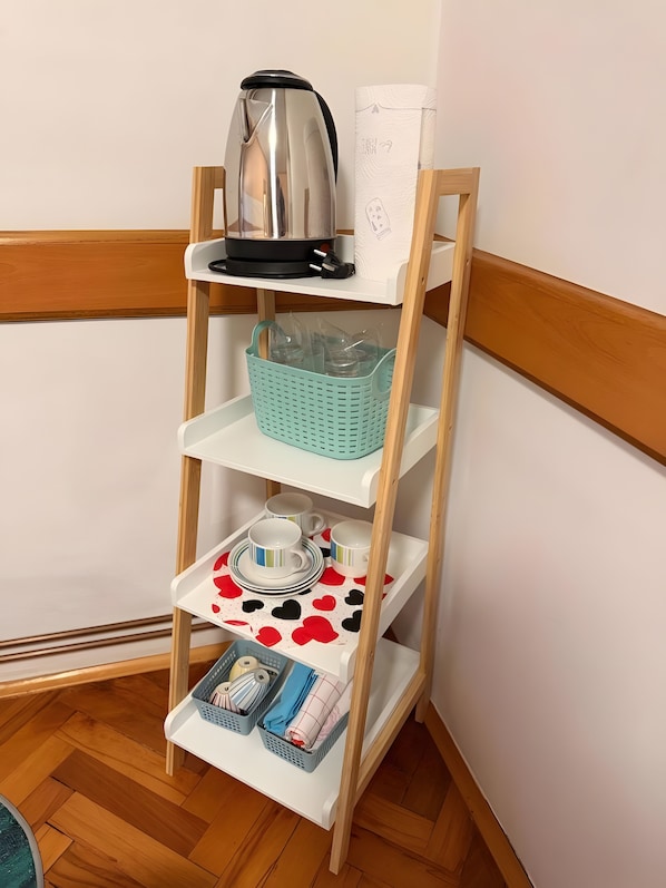 Un meuble d’angle avec une étagère, une théière, un panier et un plateau contenant des tasses et des soucoupes.