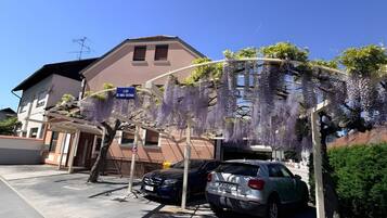 Een parkeerplaats met twee auto's, een gebouw met een bruine gevel, en een boom met paarse bloemen.