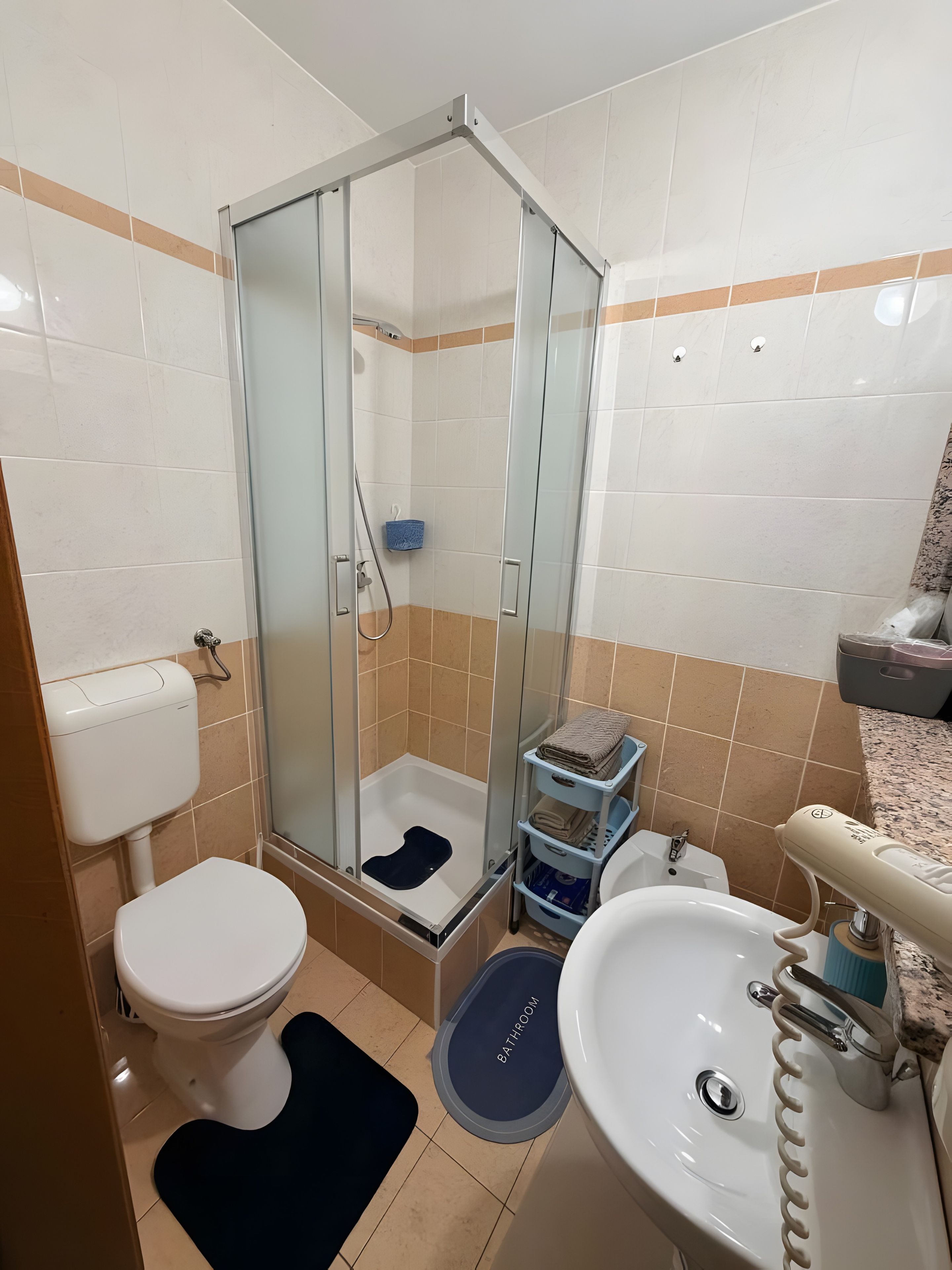 Een badkamer met toilet, wastafel, douchecabine en een opbergplank.
