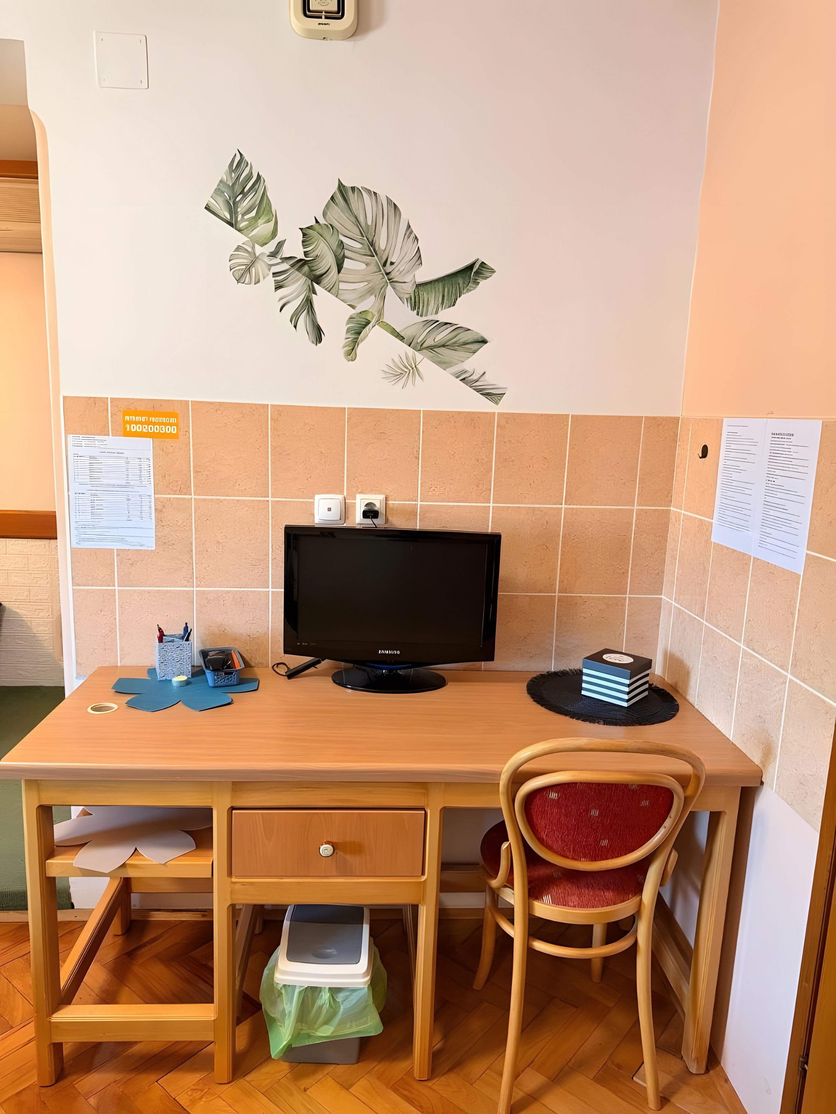 Een houten bureau met een beeldscherm, een stoel en een wanddecoratie met een plant.