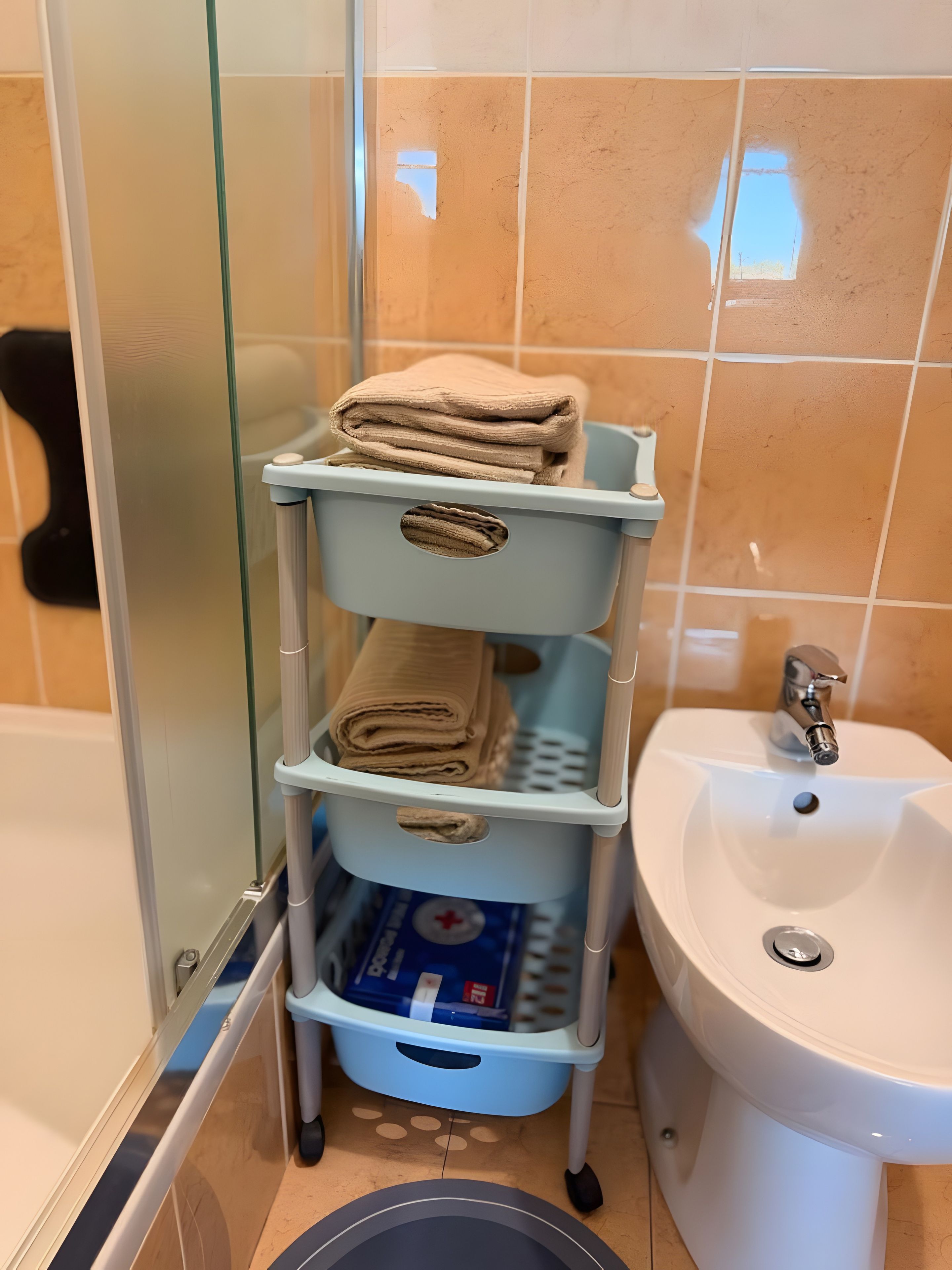 A bathroom with a glass shower enclosure, a white sink, and a blue towel rack with folded towels.