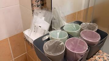 A bathroom with a tiled wall, a shower area, and a countertop with a black tray holding several cups wrapped in plastic.