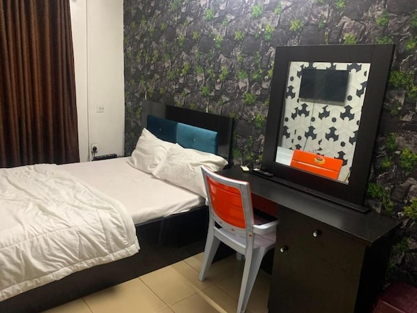 Un dormitorio con cama, escritorio y silla. Hay un televisor montado en la pared y un cuadro enmarcado.