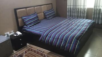 Una cama con una colcha a rayas, una mesita de noche con un teléfono y papeles, y una ventana con cortinas.