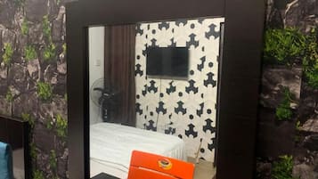 Un dormitorio con una cama, un televisor montado en la pared y un espejo que refleja la habitación.