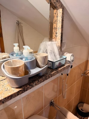 Une salle de bain avec un comptoir où sont posés les articles de toilette, un sèche-cheveux et un porte-serviettes.
