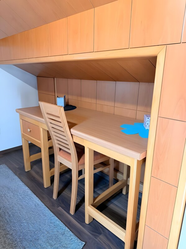 Une petite pièce en bois, avec un bureau et une chaise, un tapis bleu sur le sol et un mur blanc.