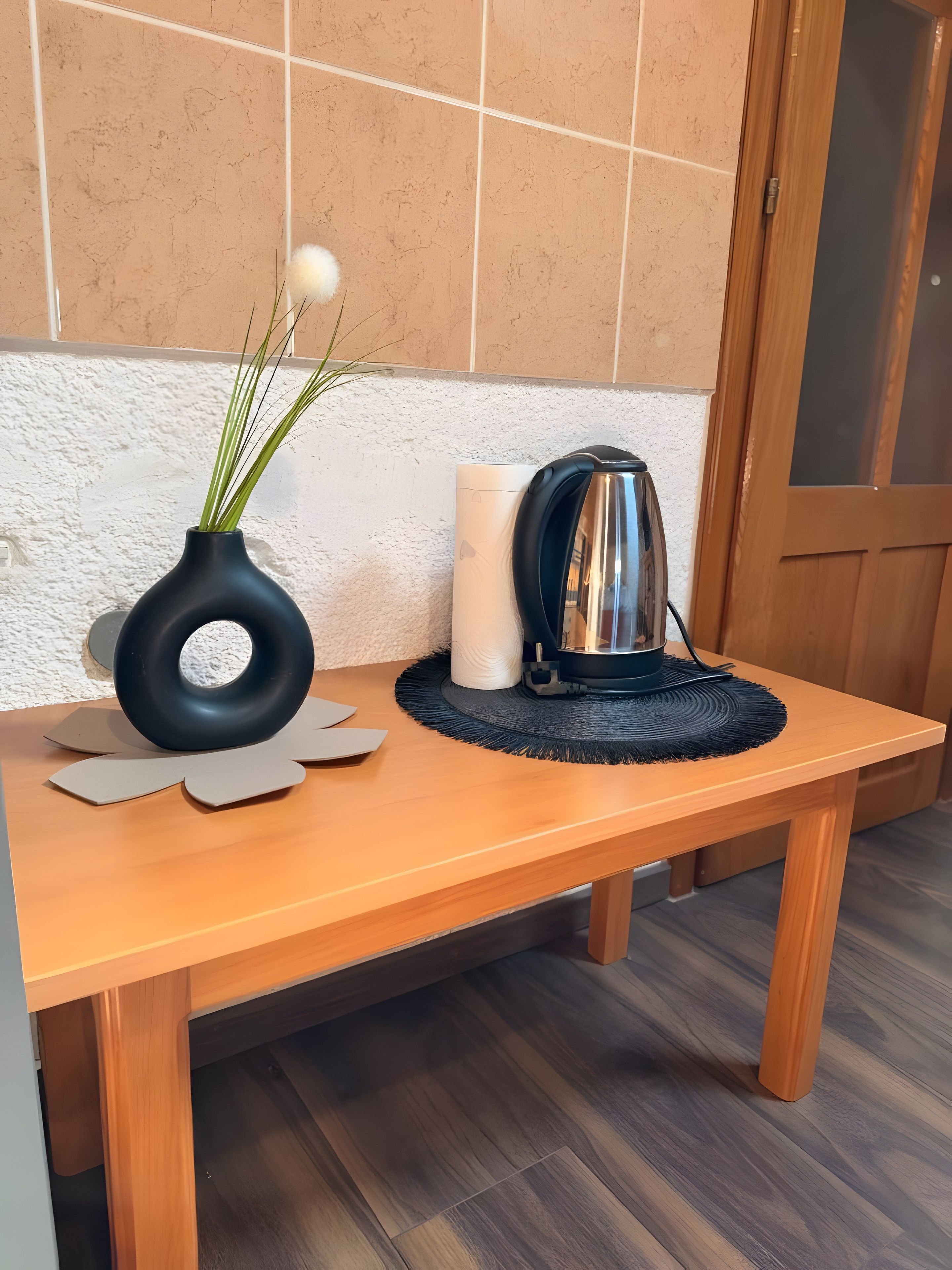 A wooden table with a vase of green plants and a kettle.