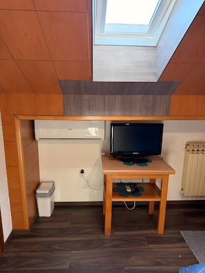 Une pièce de taille modeste, comprenant un bureau en bois, un téléviseur et une petite poubelle.