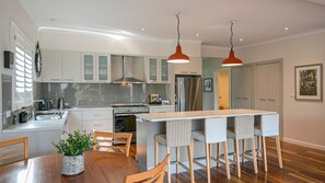 A modern kitchen with a central island, stainless steel appliances, and a dining area with wooden chairs. - Gecko at 121 the getaway you have been wanted (Werri Beach)