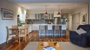 A modern kitchen with a central island, wooden dining table, and bar stools. - Gecko at 121 the getaway you have been wanted (Werri Beach)