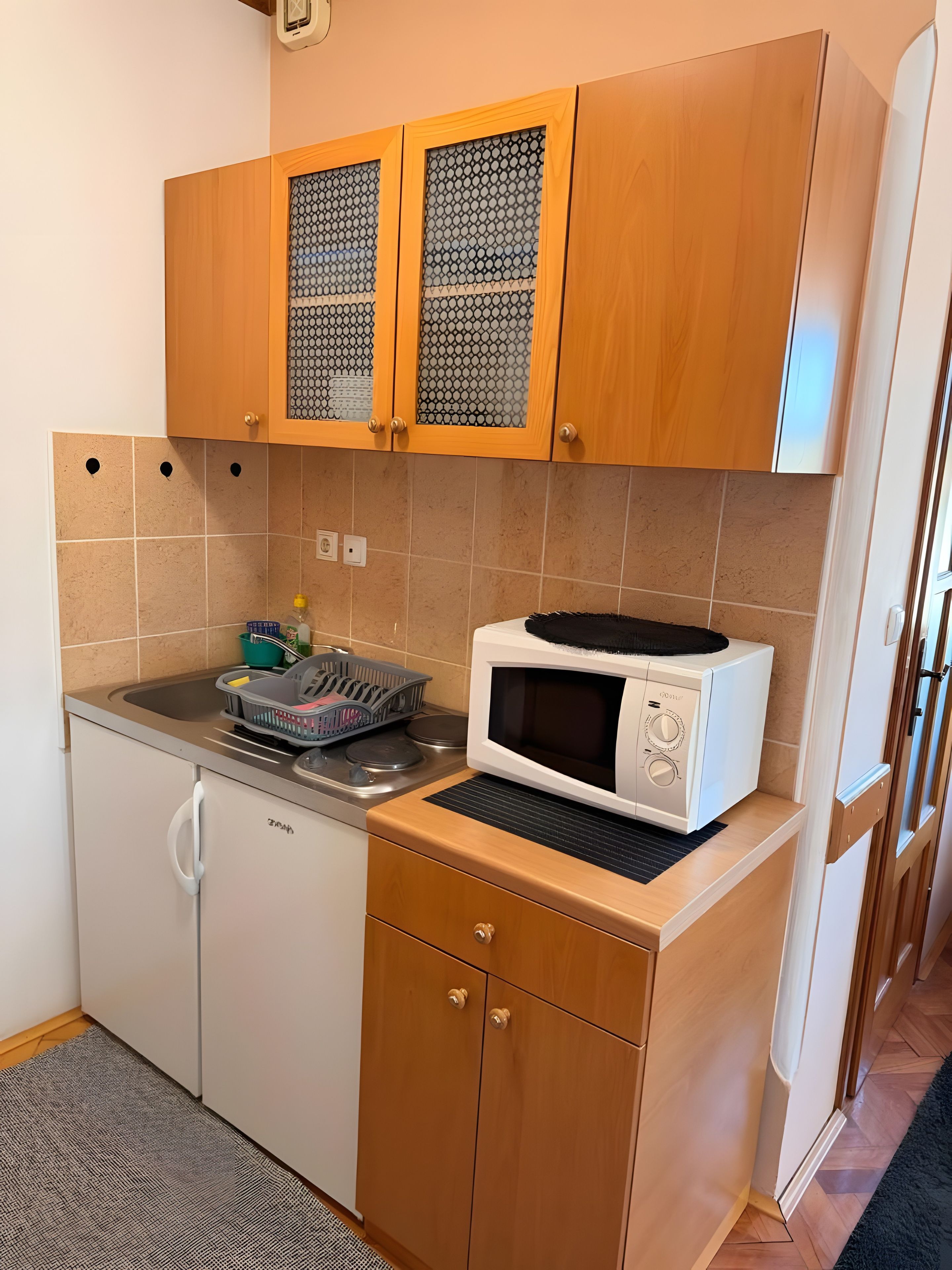 A compact kitchen with wooden cabinets, a microwave, and a dish rack.