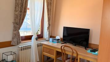 Ett rum med ett skrivbord i trä, en tv, en stol, ett element och ett fönster med gardiner.