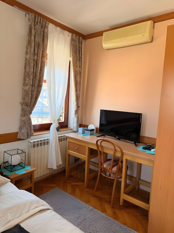 Una habitación con un escritorio de madera, televisión, silla, radiador y ventana con cortinas.