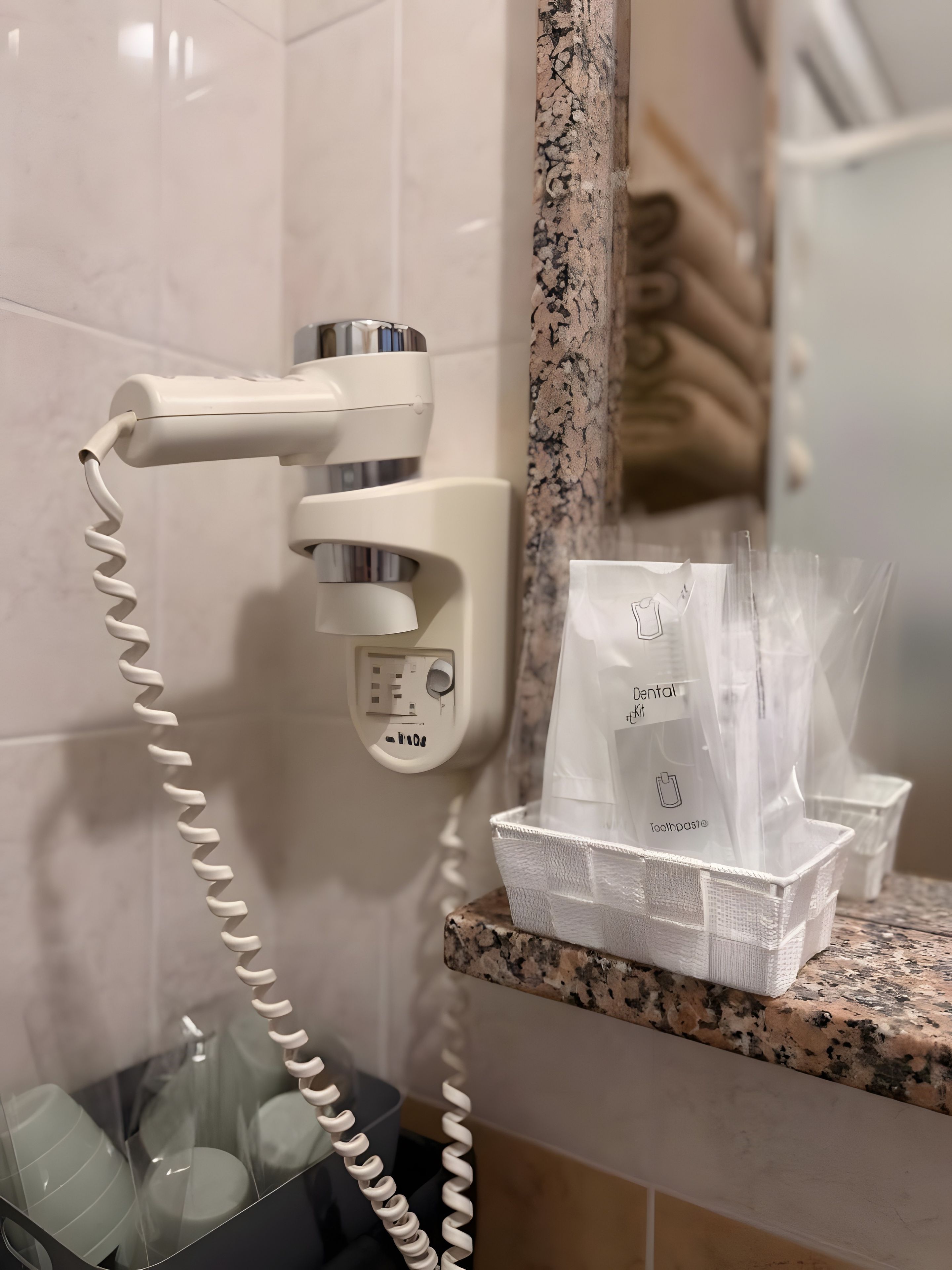 A hair dryer mounted on a wall, a mirror, and a tray with dental care items.
