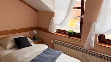 Ein Schlafzimmer mit einem Bett, einem Nachttisch, einem Fenster mit Vorhängen, einer Heizung und einer Wandpflanze.