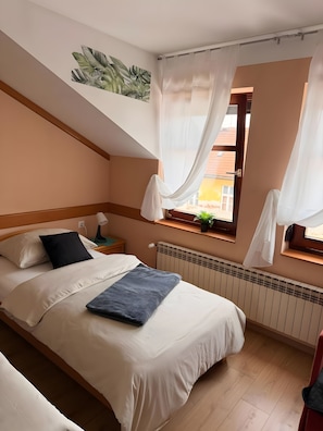 Ein Schlafzimmer mit einem Bett, einem Nachttisch, einem Fenster mit Vorhängen, einer Heizung und einer Wandpflanze.