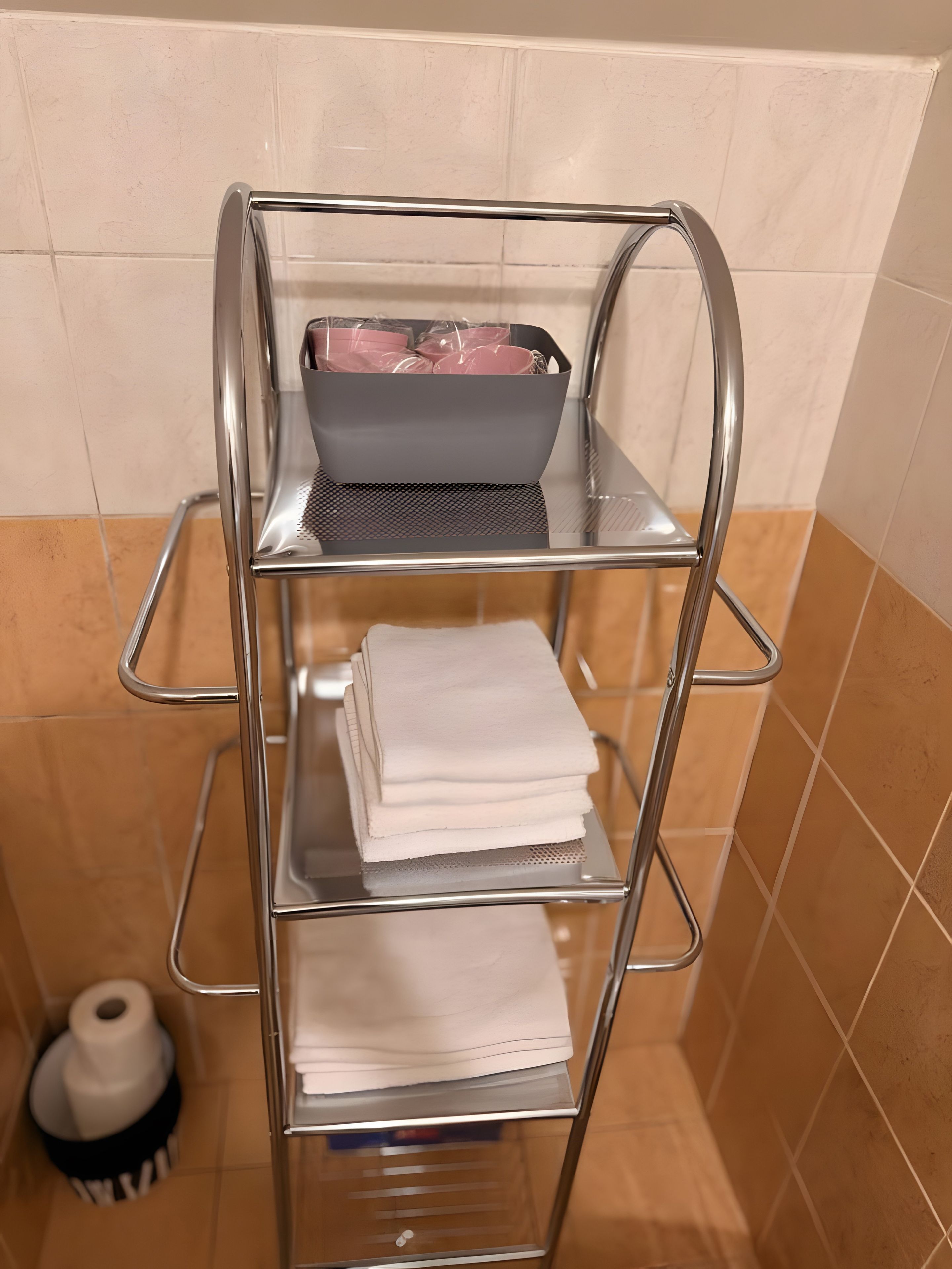 Une étagère métallique à plusieurs niveaux, sur laquelle sont pliés des serviettes et posé un panier contenant des articles roses.