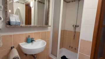 A bathroom with a sink, mirror, shower, and a towel rack.