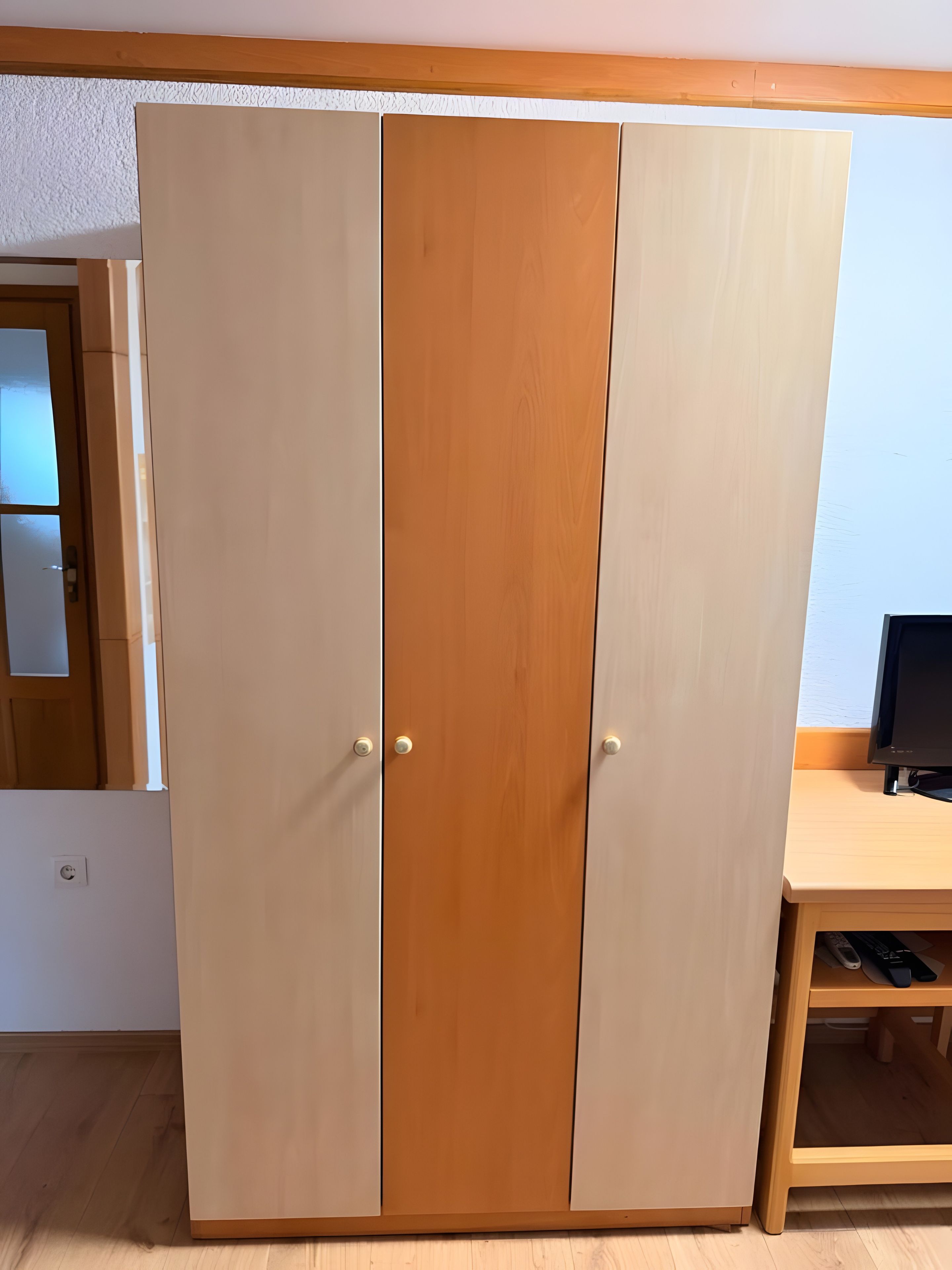 Een kamer met een garderobe, bureau en televisie.